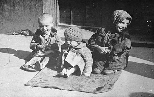 young children sit on the pavement in the Warsaw ghetto